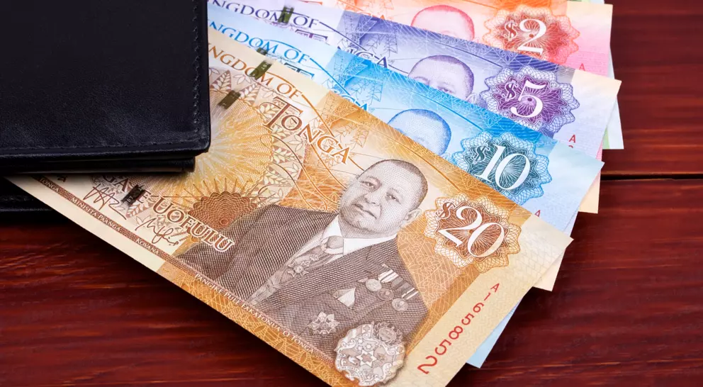 A wallet with Tongan banknotes in various denominations displayed on a wooden surface.