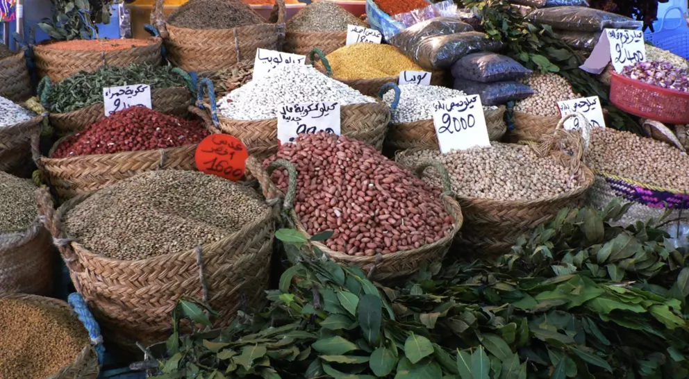 Baskets of colorful spices and legumes arranged in a market, with price tags visible in Arabic.