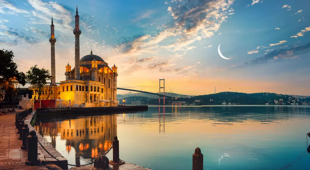 View of Ortakay Mosque in Istanbul with the Bosporus Bridge and the moon in the sky.