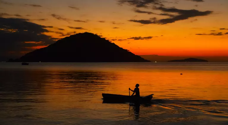 Fisherman on boat at sunset in lake