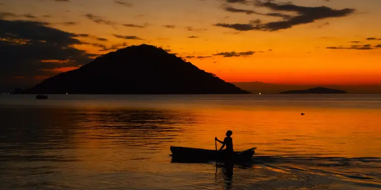 Fisherman on boat at sunset in lake