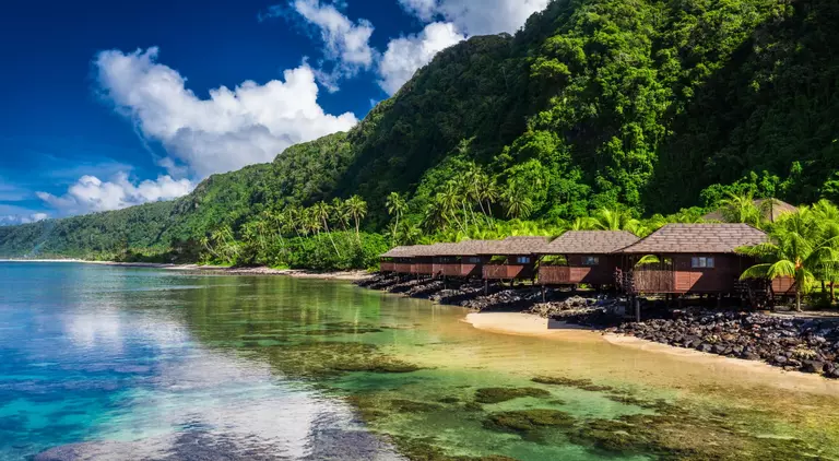 Small beach houses line the shore with green vegetation behind them