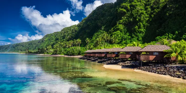 Small beach houses line the shore with green vegetation behind them