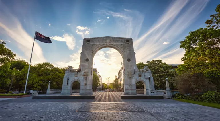 Sunset Panorama of the famous Bridge of Remembrance in Christchurch with New Zealand Flag blowing in the wind. Arch backlit against the sunset Sun