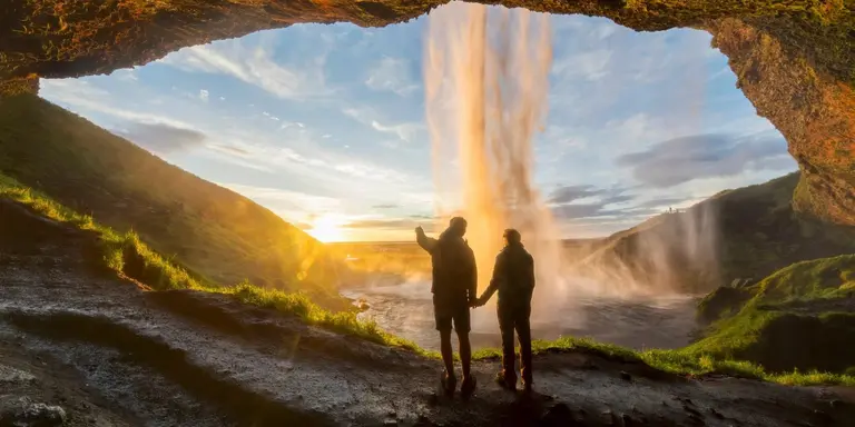 Tourists under waterfall in Seljalandsfoss, Iceland, man pointing with finger to the sun