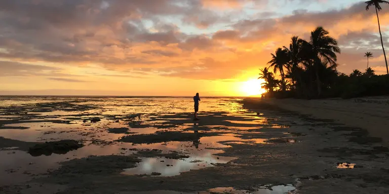 a man walks across the beaches of Vanua Levu, Fji at sunset as the sun is about to dip beneath the horizon