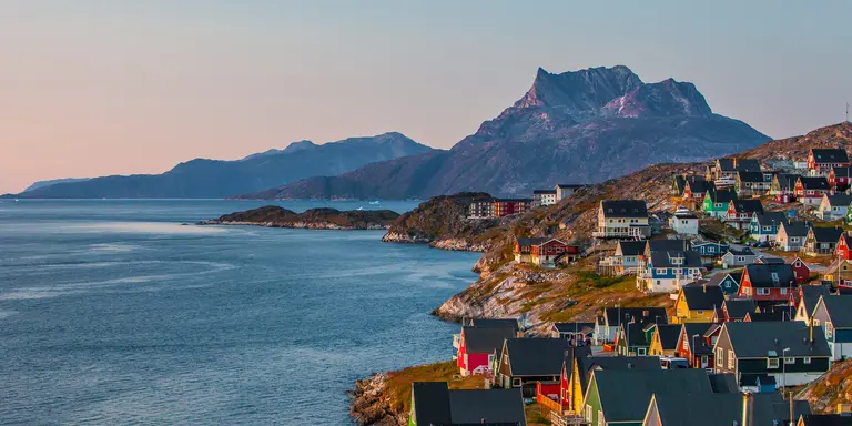 A coastal view of the Greenlandic capital of Nuuk with its colourful homes lining the edge of the water and backdrop of mountains.