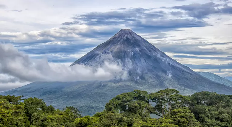 Rainforest, volcano rising in distance with clouds surrounding