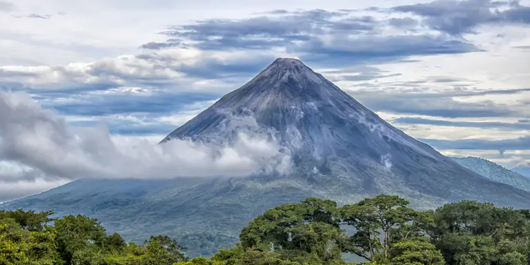 Rainforest, volcano rising in distance with clouds surrounding