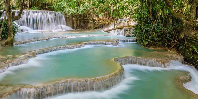 The Kuang Si Falls begin in shallow pools atop a steep hillside. The water flows in to a turquoise blue pool