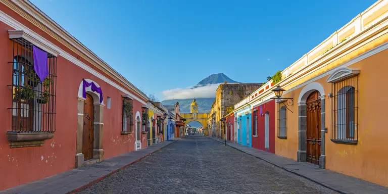 "Colorful main street of Antigua city at sunrise with the famous yellow arch and the Agua volcano in the background "