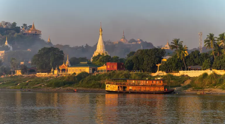 Landscape of Myanmar from the river just after sunrise. Warm colors, lots of pagoda's and a steamboat