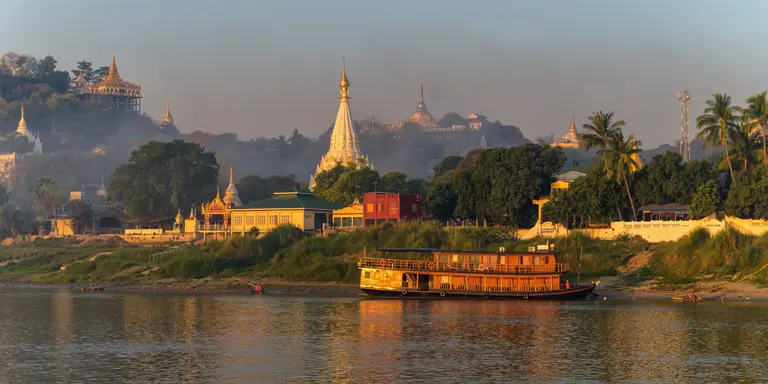 Landscape of Myanmar from the river just after sunrise. Warm colors, lots of pagoda's and a steamboat