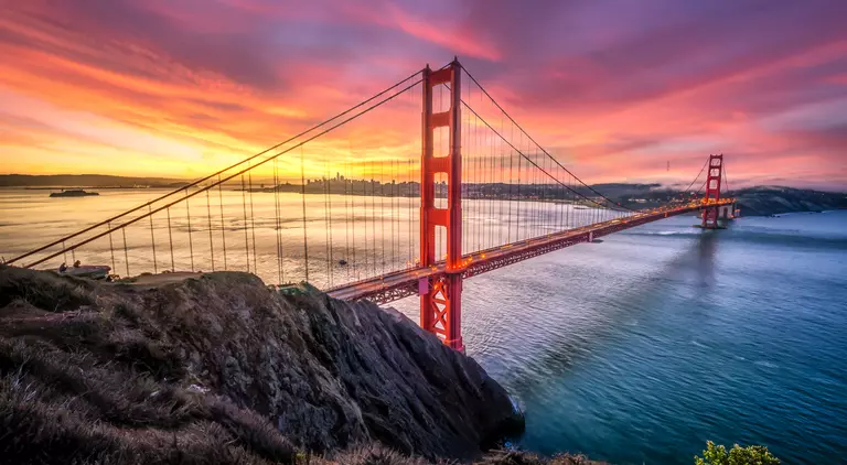Colored sunrise with wide shot of bridge and city in the background