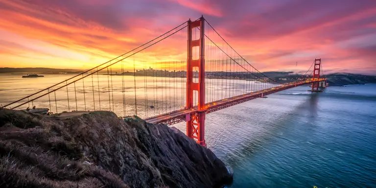 Colored sunrise with wide shot of bridge and city in the background
