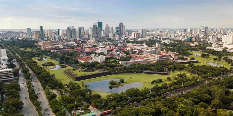 Aerial of Intramuros, an old historic walled city, surrounded by golf courses, and Manila skyline in background