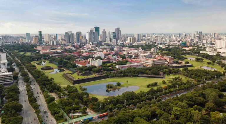 Aerial of Intramuros, an old historic walled city, surrounded by golf courses, and Manila skyline in background