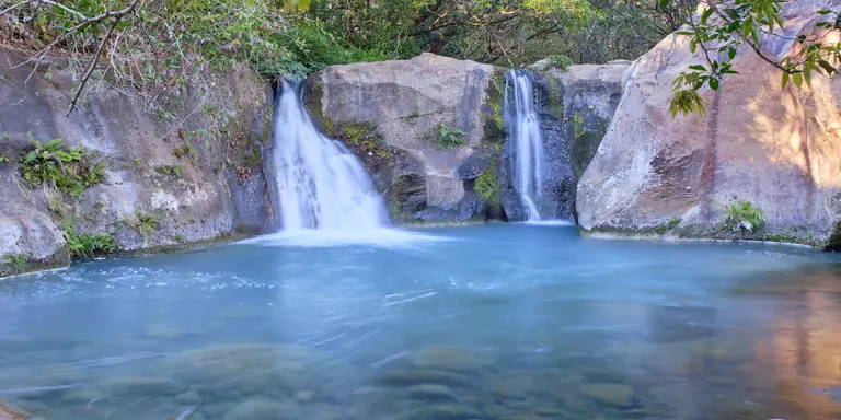 Beautiful blue logoon are surrounded by volcanic rock walls and green foliage