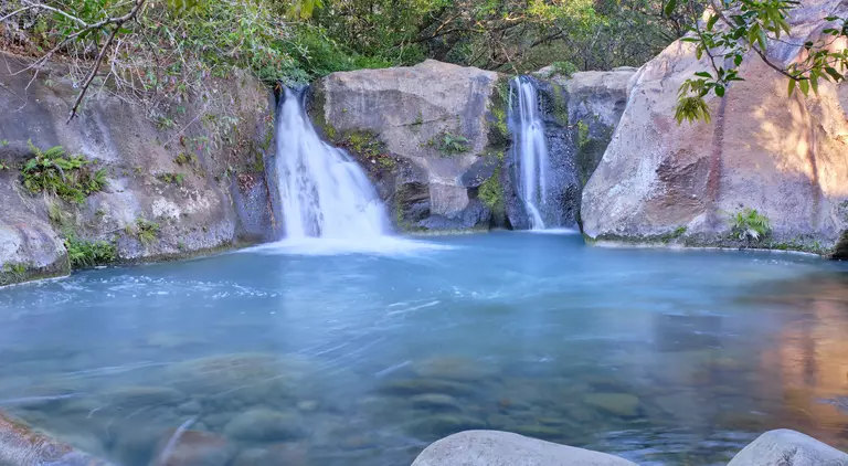 Beautiful blue logoon are surrounded by volcanic rock walls and green foliage