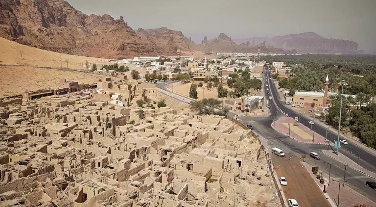 "Elevated view Al-Ula centuries-old mudbrick heritage site, lush green date palm groves, and sandstone rock formations "