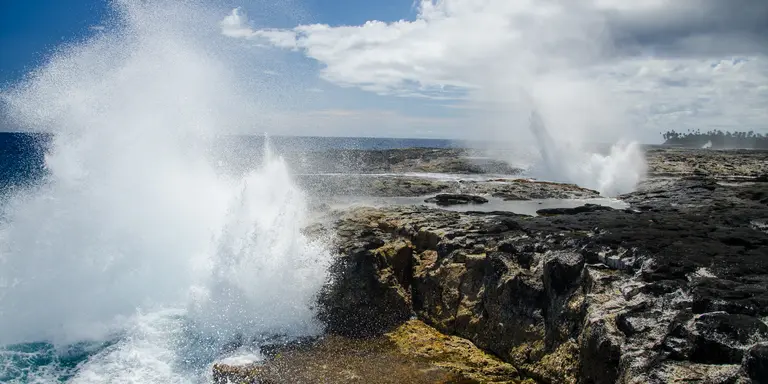 The Alofaaga Blowholes send water towards the bright blue sky along the ocean in Somoa