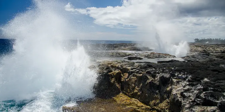 The Alofaaga Blowholes send water towards the bright blue sky along the ocean in Somoa