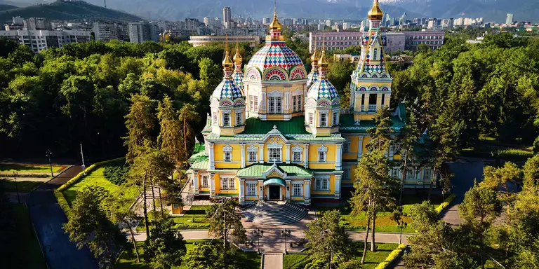 Aerial view of the Zenkov Cathedral in Panfilov Park against blue sky and and snowy mountains in Almaty city, Kazakhstan