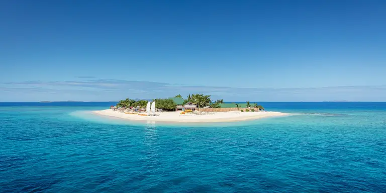 Beautiful small island in the middle of the south pacific ocean with beach huts, lounge chairs, palm trees, surrounded with beautiful clear turquoise water.