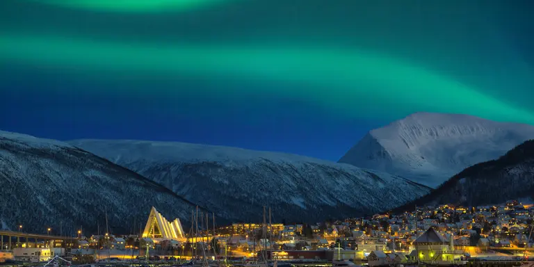 View at night on illuminated Tromso city with cathedral and majestic aurora borealis
