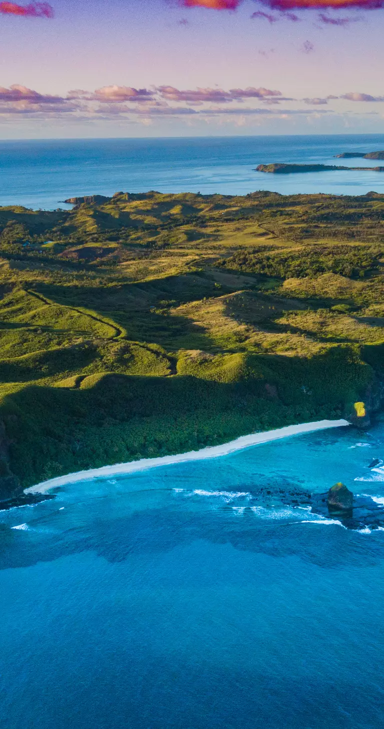 Aerial view of a Fiji island with bright green foliage and sunset sky
