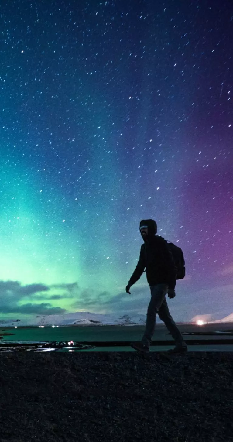 Solo traveler walking in front of an awesome Northern Lights in Mount Kirkjufell Iceland.