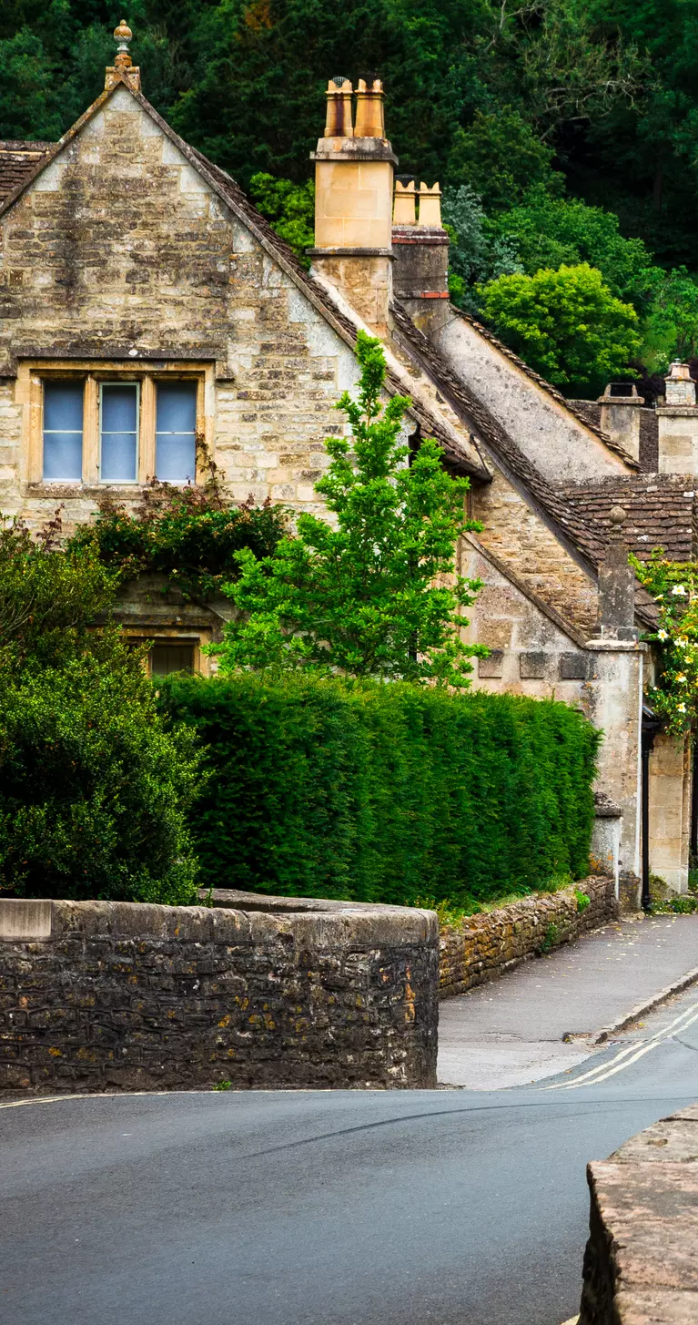 Traditional English village in the Cotswolds area of southwest England. The cosy little brick cottages line the narrow road, and there is also a quaint bridge spanning a little stream.