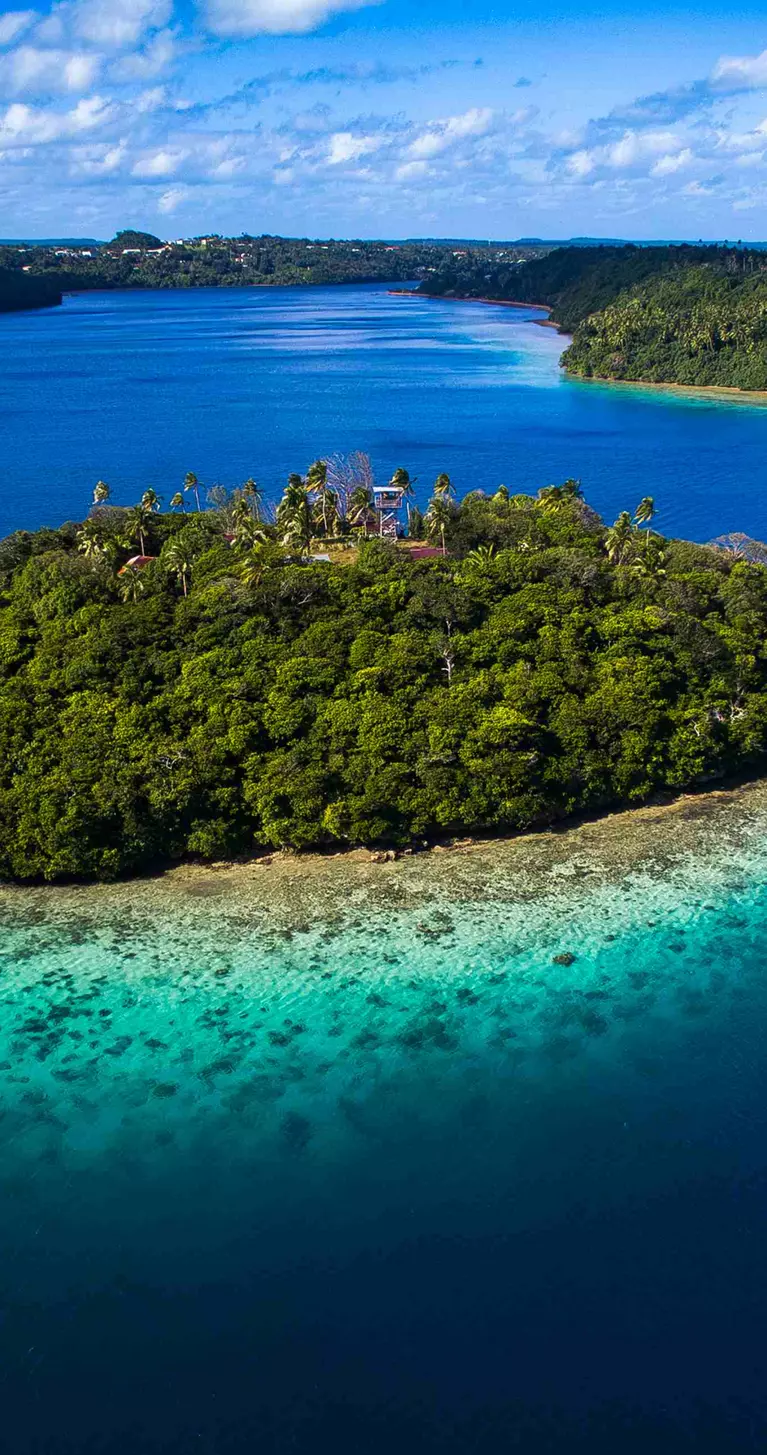 Aerial view of tiny tropical island surrounded by pristine blue water and coral reef in Tonga