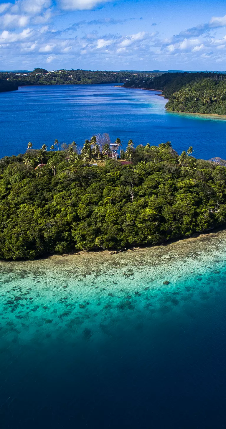 Aerial view of tiny tropical island surrounded by pristine blue water and coral reef in Tonga