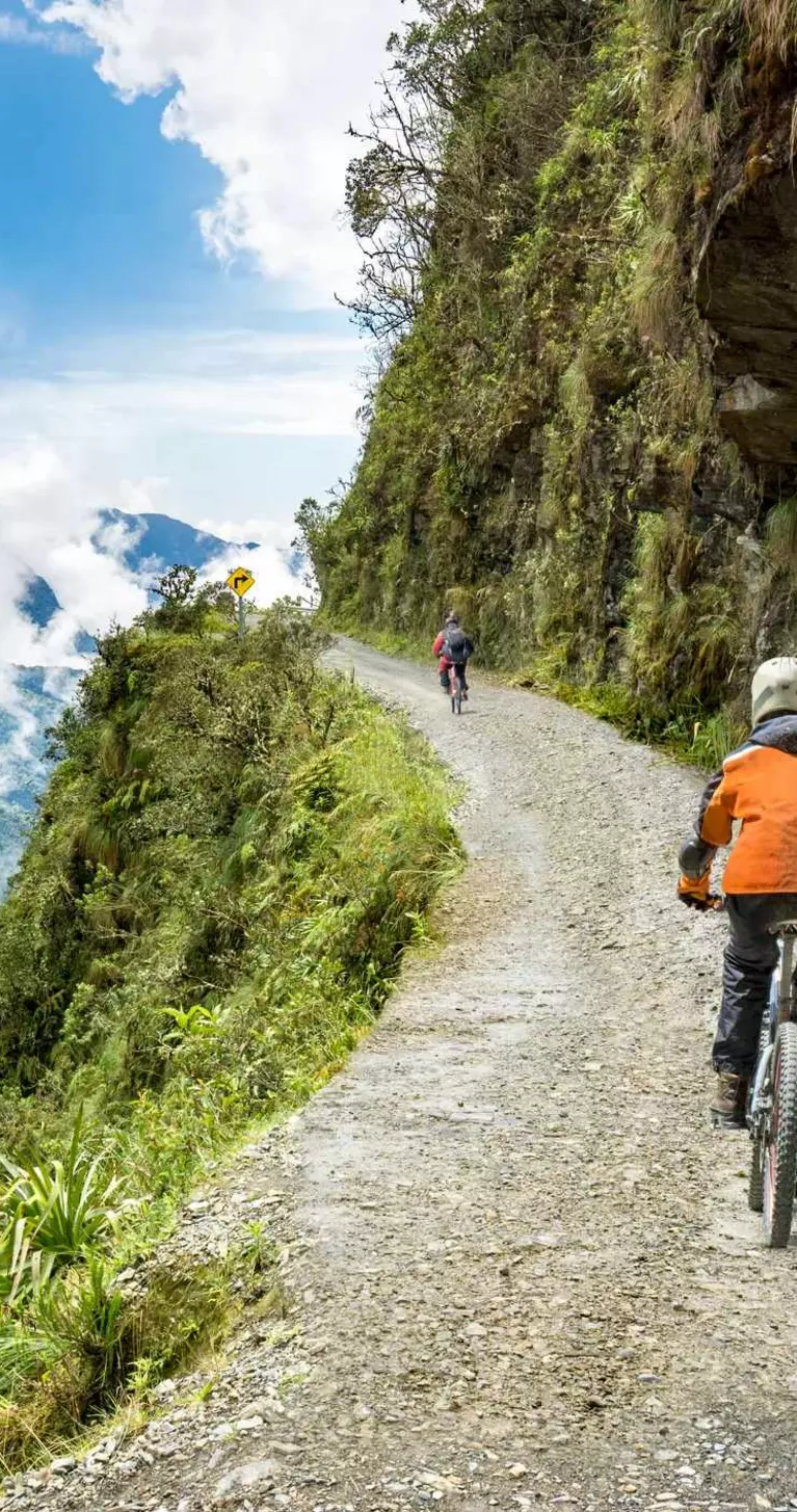 Bike tourists ride on North Yungas road, known as "Death Road" in Bolivia. In the background sky circles a condor over the scene.