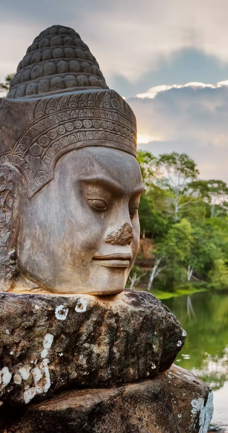 Stone face Asura over moat on causeway near South Gate of Angkor Thom in Siem Reap, Cambodia