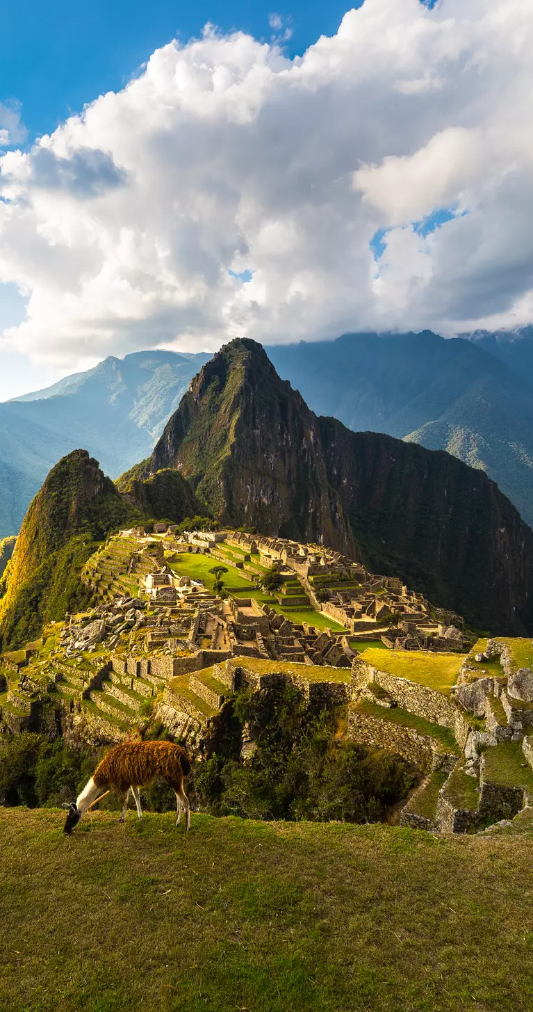 Machu Picchu illuminated by the warm sunset light. Wide angle view from the terraces above with scenic sky and sun burst