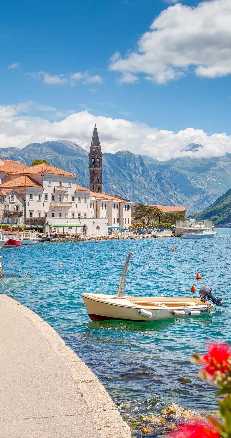 Panorama view of Perast at famous Bay of Kotor with blooming flowers on a beautiful sunny day with blue sky and clouds in summer
