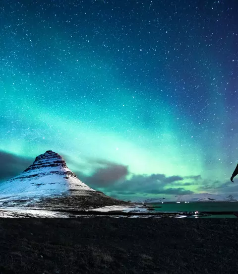 Solo traveler walking in front of an awesome Northern Lights in Mount Kirkjufell Iceland.