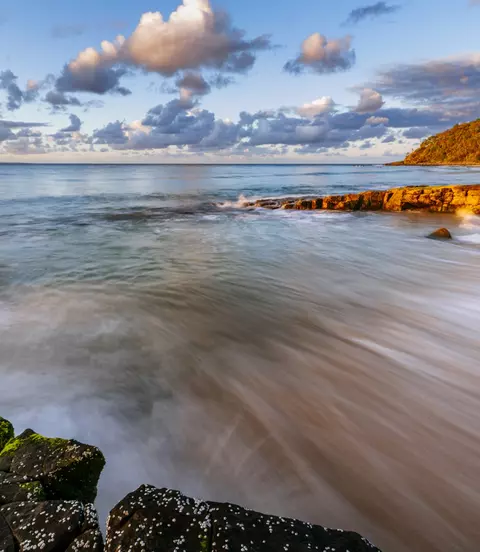 Water crests the shoreline at sunset
