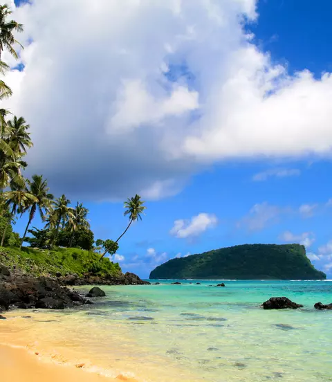 Tropical seascpape, golden sandy beach with palm trees and pristine blue waters of Pacific Ocean, view from Upolu to Nu'utele Island