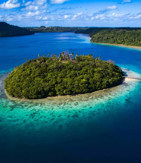 Aerial view of tiny tropical island surrounded by pristine blue water and coral reef in Tonga