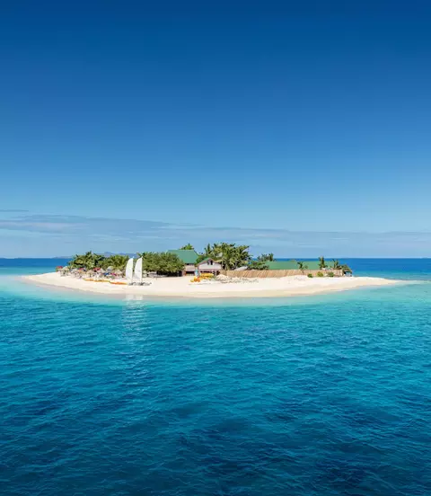 Beautiful small island in the middle of the south pacific ocean with beach huts, lounge chairs, palm trees, surrounded with beautiful clear turquoise water.