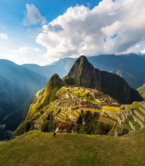 Machu Picchu illuminated by the warm sunset light. Wide angle view from the terraces above with scenic sky and sun burst