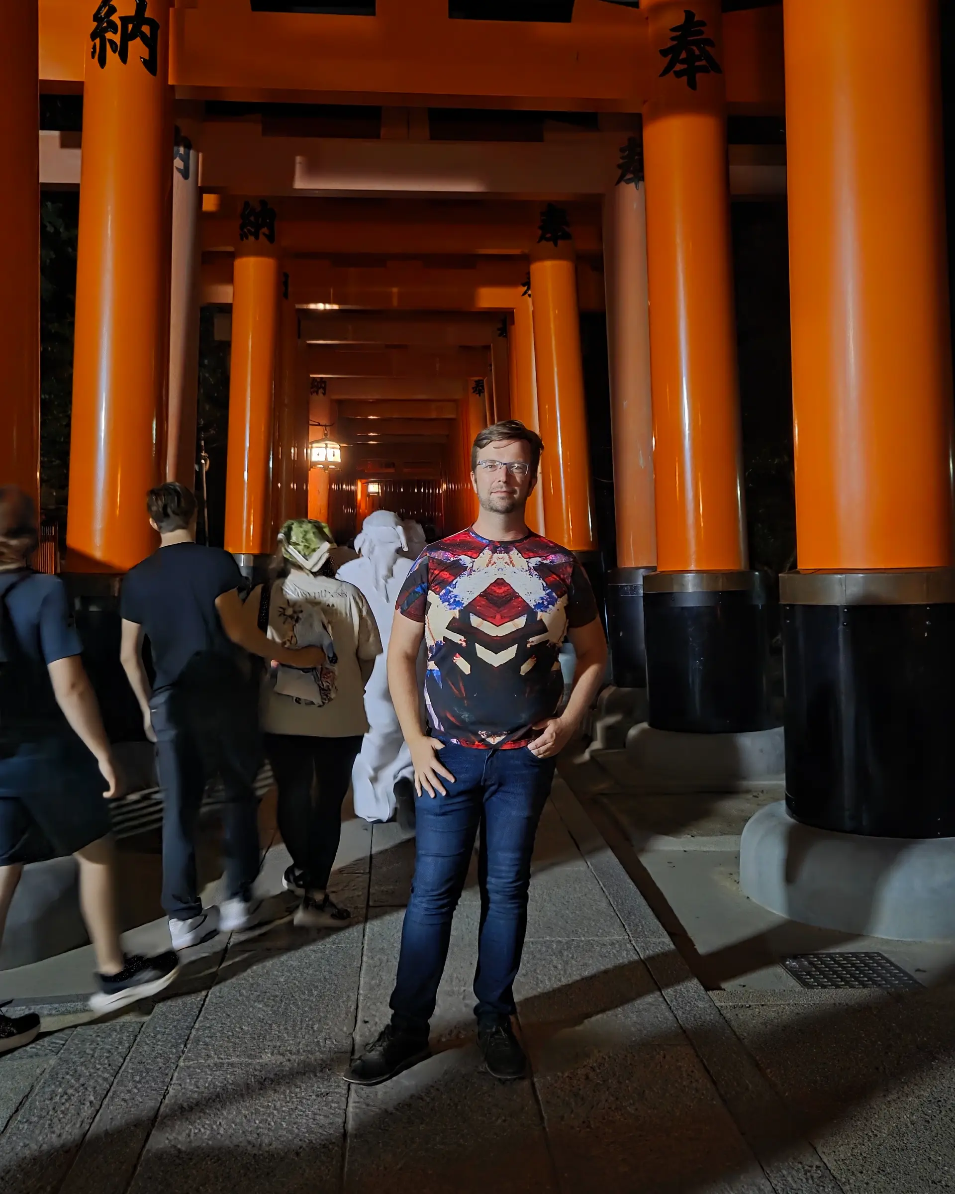 Globetrotting writer Christian standing beneath the orange torii gates of Fushimi Inari Taisha Shrine in Kyoto, Japan, at night