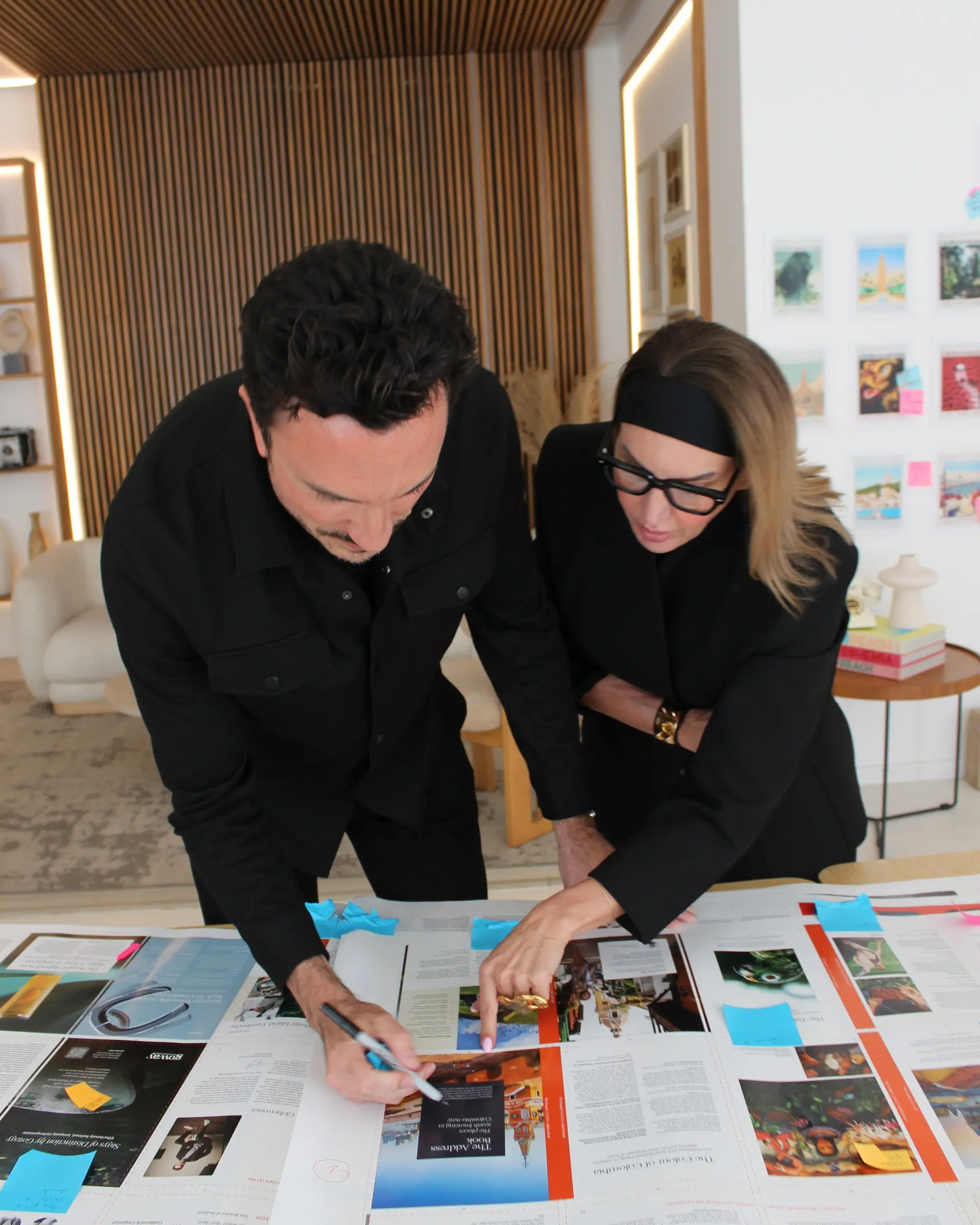 Globetrotting Editor in chief Mitchell Alexander reviewing printed page proofs of Vol. 38 on a table, marking edits with a Sharpie and blue Post-it notes