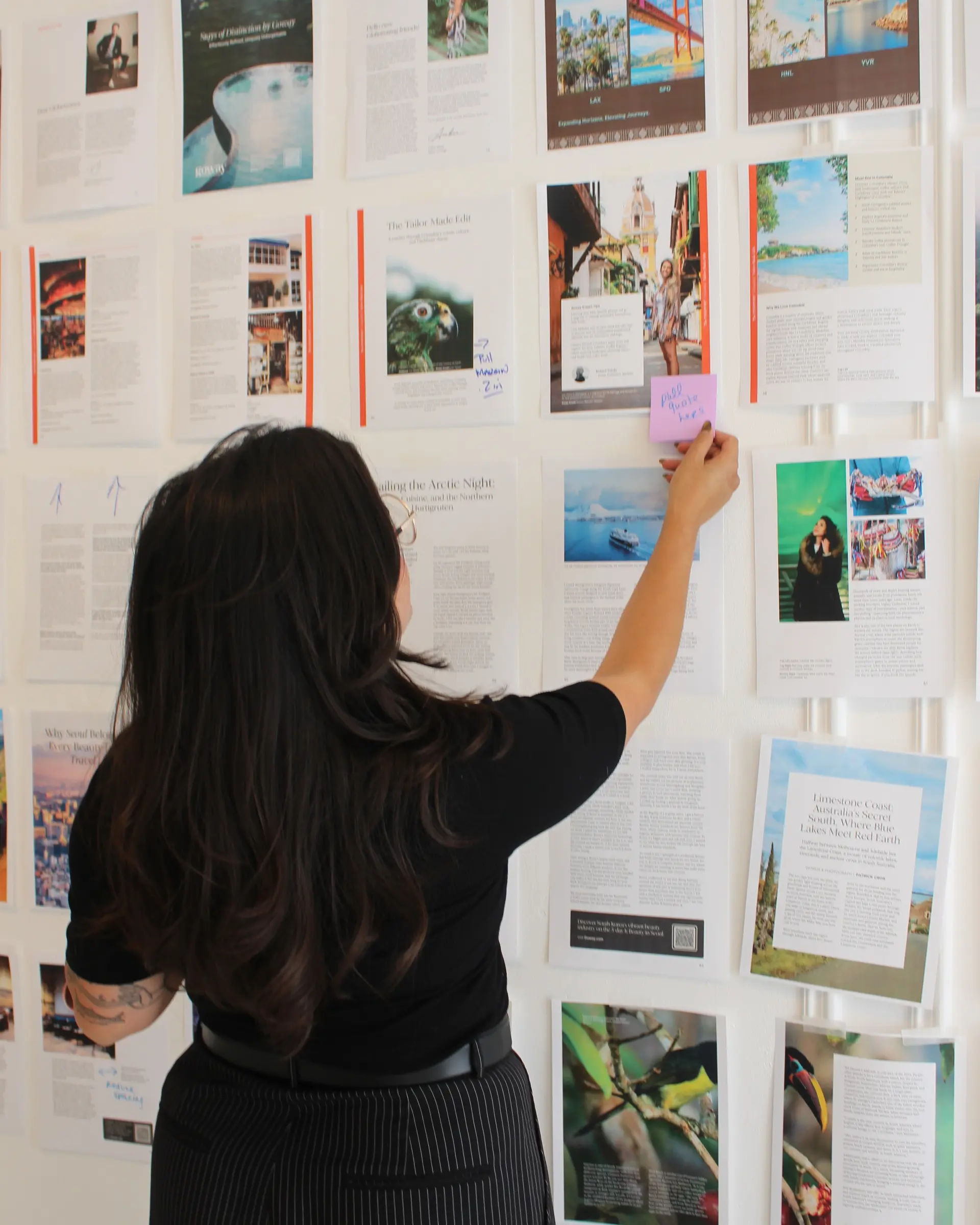 Globetrotting team member adding a "pull quote here" Post-it note to the pagination wall of draft travel magazine layouts