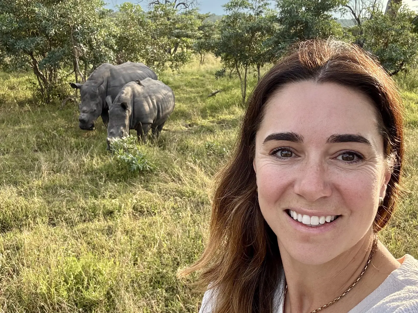 Bronwyn Hodge smiling in front of two rhinos on a safari in Africa.