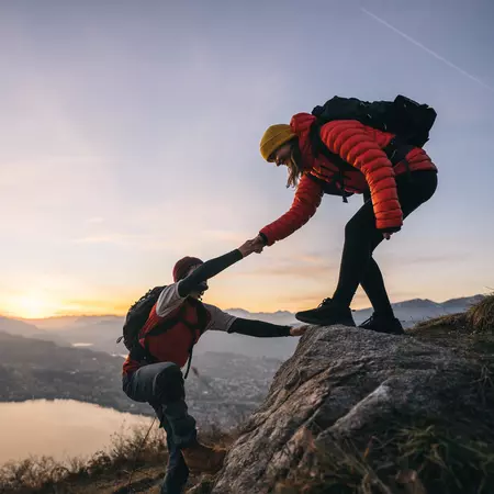 People helping one another climb a mountain