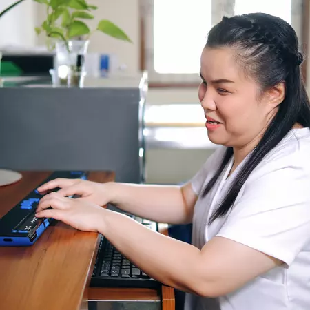 Woman with blindness disability using computer with refreshable braille display or braille terminal a technology assistive device for persons with visual impairment in workplace